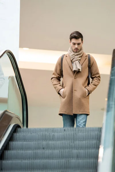 Homem bonito em roupas quentes se aproximando escada rolante no shopping — Fotografia de Stock