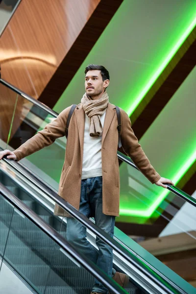 Handsome man in warm clothing going down on escalator in shopping mall — Stock Photo