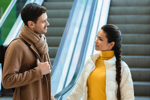 Schöner Mann und attraktives Mädchen stehen in der Nähe der Rolltreppe und schauen einander an — Stockfoto