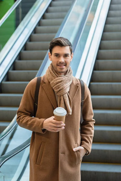 Красивий чоловік тримає одноразову чашку і посміхається на ескалаторі — стокове фото