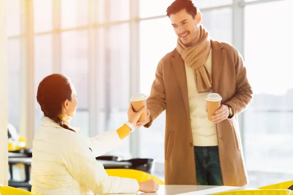 Bell'uomo che dà tazza di carta alla ragazza seduta a tavola nel caffè — Foto stock