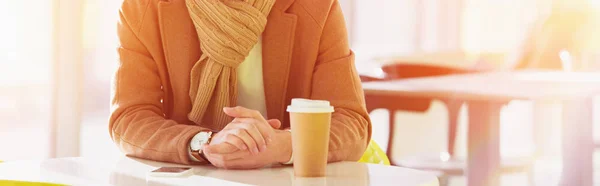 Cropped view of man sitting at table with disposable cup in cafe — Stock Photo