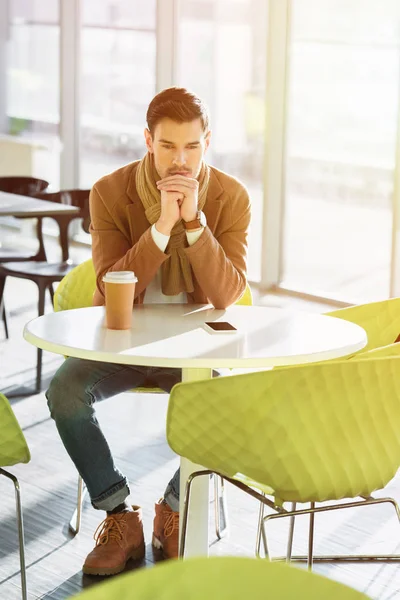 Uomo deluso seduto a tavola con tazza usa e getta e smartphone nel caffè — Foto stock