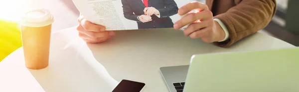 Vista recortada del hombre sentado en la mesa con el ordenador portátil y el periódico de lectura - foto de stock