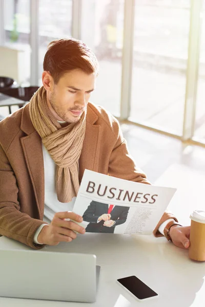 Homem de negócios sério sentado à mesa, segurando copo de papel e lendo jornal de negócios no café — Fotografia de Stock