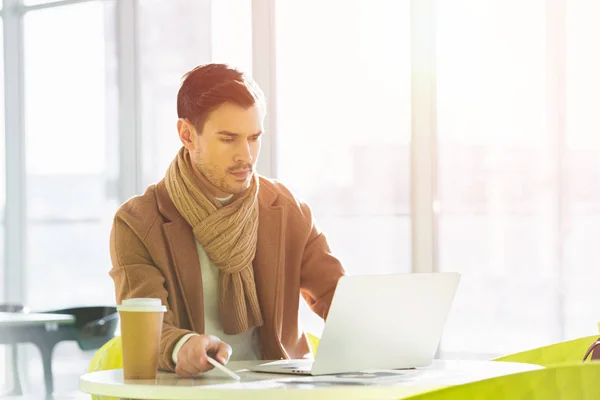 Handsome man working on laptop in light cafe — Stock Photo