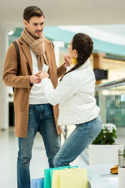 Girl in warm clothing holding hands with smiling man and getting up from bench in shopping mall — Stock Photo