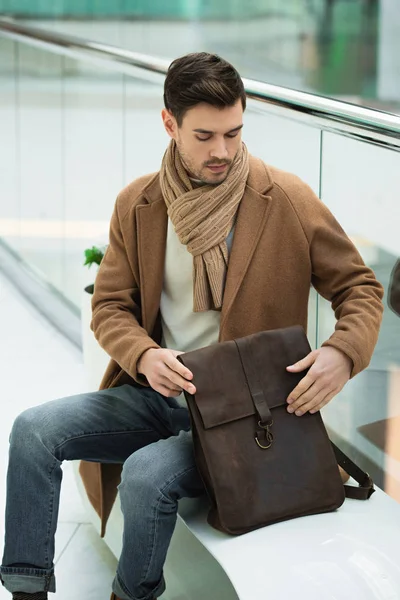 Bel homme tenant le sac et assis sur le banc — Photo de stock