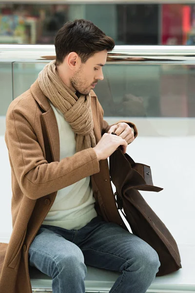 Schöner Mann sitzt auf Bank und öffnet Tasche — Stockfoto