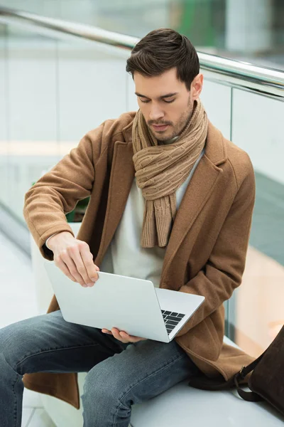 Bel homme assis sur le banc et tenant ordinateur portable — Photo de stock