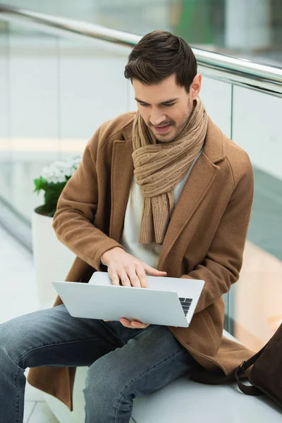 Sorrindo homem sentado no banco e digitando no teclado do laptop — Fotografia de Stock