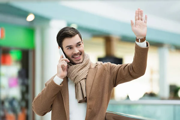 Sonriente hombre hablando en smartphone y saludando con la mano - foto de stock