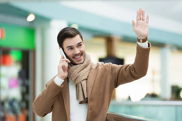 Smiling man talking on smartphone and waving with hand — Stock Photo