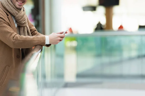 Abgeschnittene Ansicht eines Mannes in warmer Kleidung, der lächelt und sein Smartphone in der Hand hält — Stockfoto