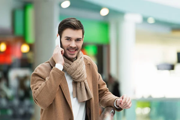 Homem bonito falando no smartphone e sorrindo no shopping — Fotografia de Stock