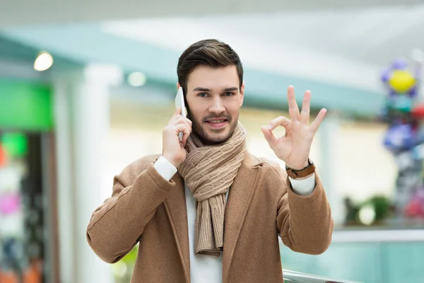 Hombre guapo hablando en el teléfono inteligente y mostrando signo ok - foto de stock