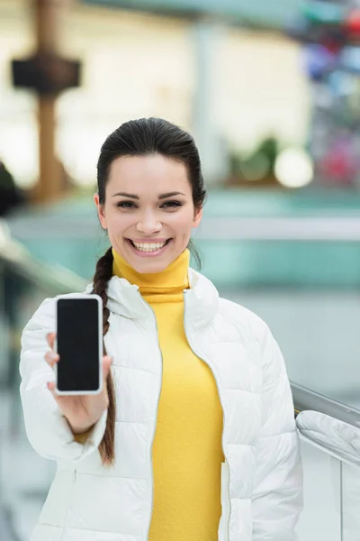 Jolie fille souriant, regardant la caméra et montrant l'écran du smartphone — Photo de stock