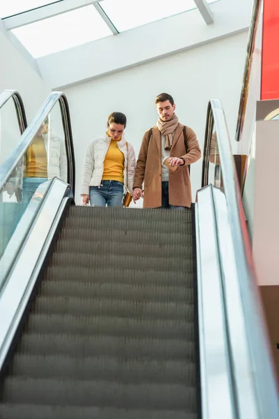 Attractive girl and handsome man standing at top of escalator — Stock Photo