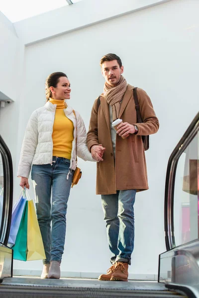 Liebespaar mit Einkaufstaschen und Einwegbecher oben auf Rolltreppe — Stockfoto