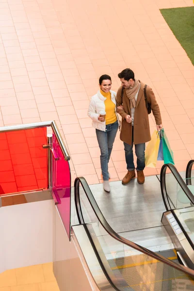 Loving couple with shopping bags near escalator in mall — Stock Photo