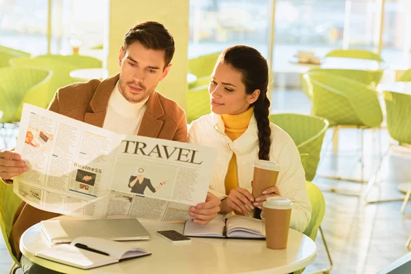 Handsome man and smiling girl reading travel newspaper in cafe — Stock Photo