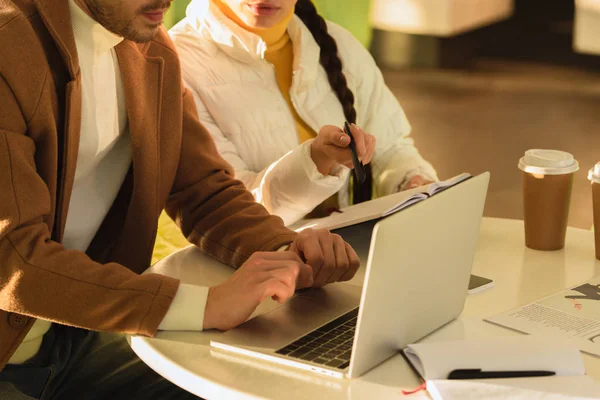 Vista recortada del hombre y la niña sentado en la mesa con el ordenador portátil en la cafetería - foto de stock