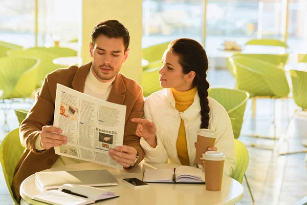 Handsome man and attractive girl reading business newspaper in cafe — Stock Photo