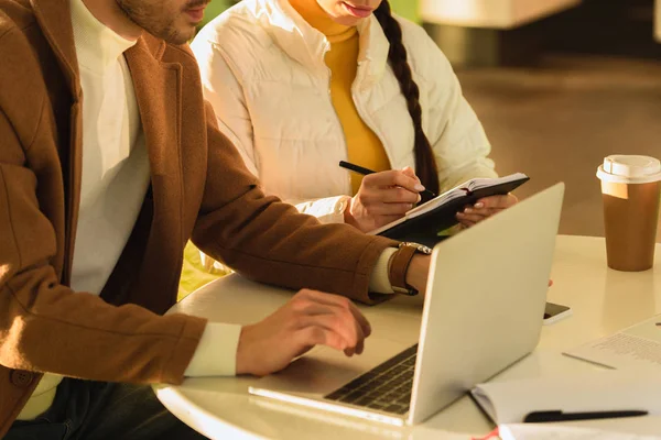 Visão cortada de homem digitando no teclado do laptop e menina escrevendo no notebook no café — Fotografia de Stock