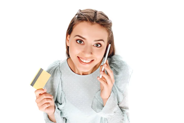 Vista de ángulo alto de la mujer sonriente con tarjeta de crédito hablando en el teléfono inteligente aislado en blanco - foto de stock