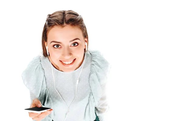 Vista ad alto angolo di donna sorridente con smartphone ascoltare musica in auricolari isolati su bianco — Foto stock