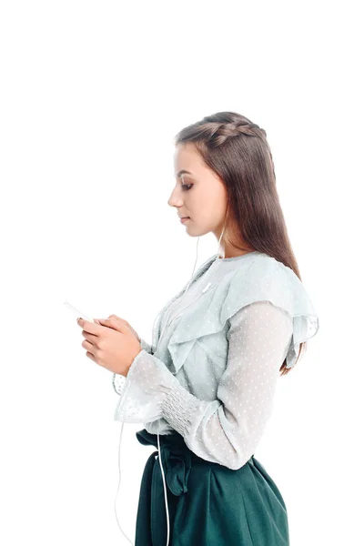 Vista laterale di giovane donna utilizzando smartphone durante l'ascolto di musica in auricolari isolati su bianco — Foto stock