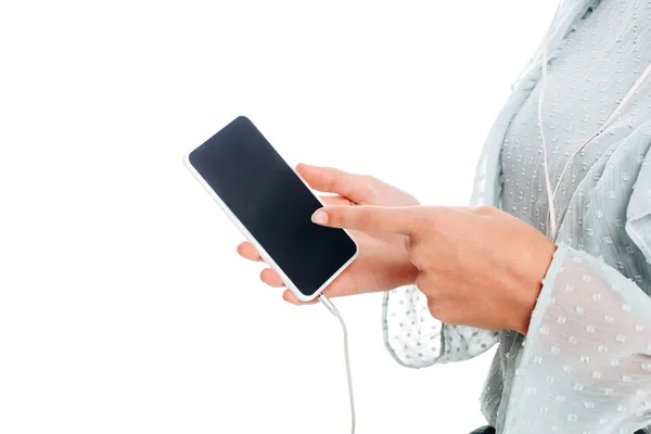 Partial view of woman pointing at smartphone while listening music in earphones isolated on white — Stock Photo