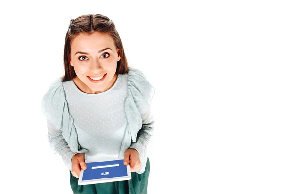 Vista ad alto angolo di donna sorridente con tablet con logo facebook sullo schermo isolato su bianco — Foto stock