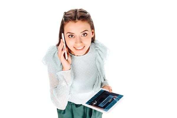 Високий кут зору усміхненої жінки з планшетом, що говорить на смартфоні ізольовано на білому — стокове фото