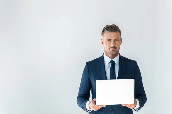 Handsome businessman holding laptop and looking at camera isolated on white — Stock Photo