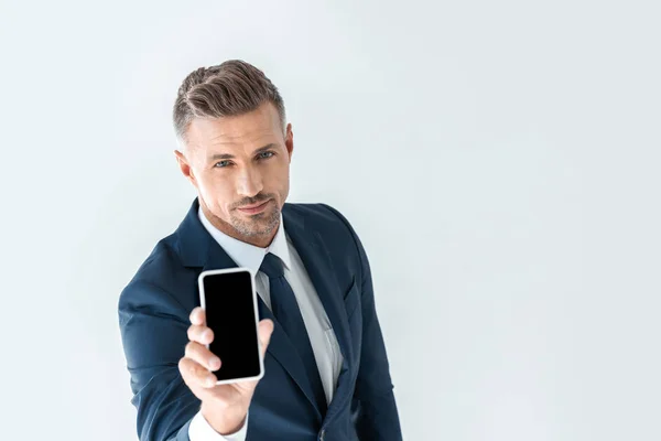 Vista ad alto angolo di bello uomo d'affari che mostra smartphone con schermo vuoto e guardando la fotocamera isolata su bianco — Foto stock