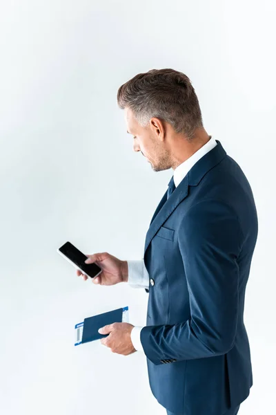 Vista de ángulo alto de hombre de negocios guapo usando teléfono inteligente con pantalla en blanco y la celebración de pasaporte con billete aislado en blanco - foto de stock