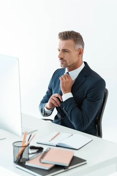 Bonito empresário amarrando gravata na mesa com computador isolado no branco — Fotografia de Stock