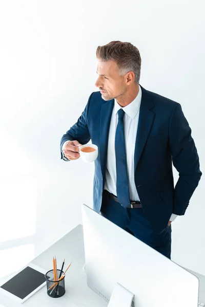 Hochwinkelige Ansicht des gutaussehenden Geschäftsmannes, der eine Tasse Kaffee hält und isoliert auf weißem Grund wegschaut — Stockfoto