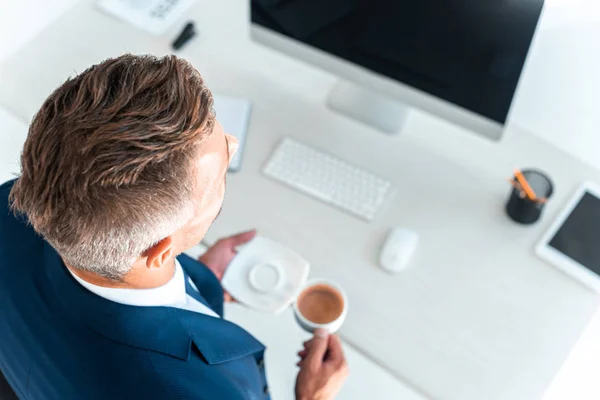 High angle view of businessman holding cup of coffee and plate near table in office — Stock Photo