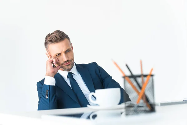 Вибірковий фокус втомленого бізнесмена, що сидить за столом з канцелярськими приладдям ізольовані на білому — стокове фото