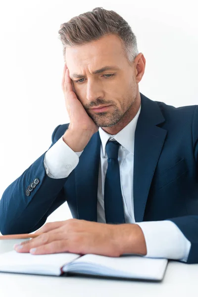 Tired handsome businessman looking at notebook isolated on white — Stock Photo