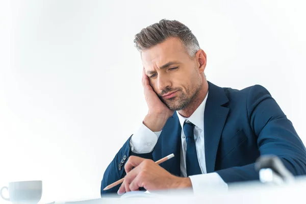 Vista de ángulo bajo del hombre de negocios cansado sosteniendo el lápiz y mirando hacia abajo en la mesa aislada en blanco - foto de stock