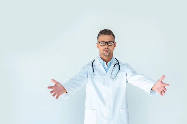 Красивий лікар в окулярах зі стетоскопом на плечах, що стоїть з відкритими руками і дивиться на камеру ізольовано на білому — стокове фото