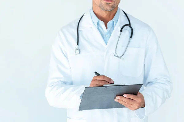 Abgeschnittenes Bild eines Arztes mit Stethoskop auf den Schultern, der etwas in die Zwischenablage schreibt, isoliert auf weiß — Stockfoto