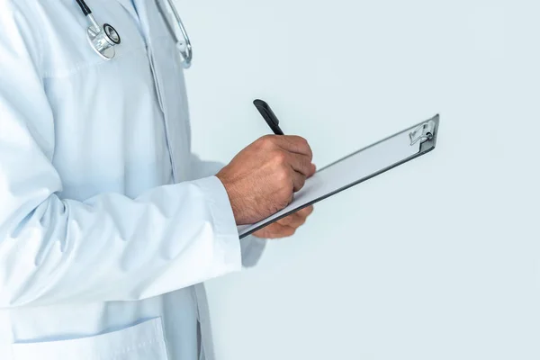 Cropped image of doctor with stethoscope on shoulders writing something in clipboard isolated on white — Stock Photo