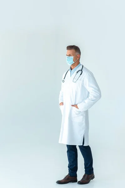 Adult doctor in white coat and medical mask looking away isolated on white — Stock Photo