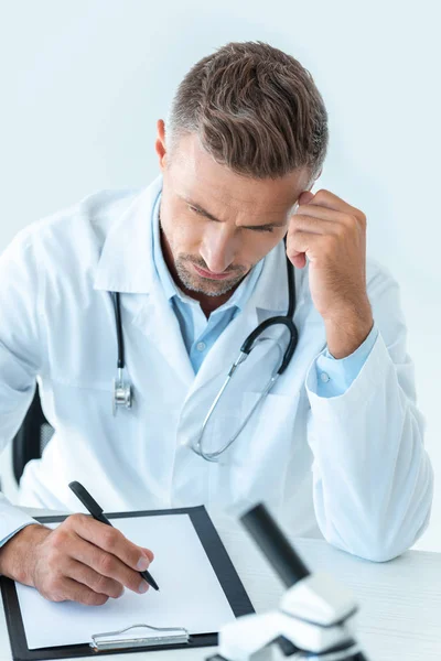 Pensive handsome scientist writing something to clipboard isolated on white — Stock Photo