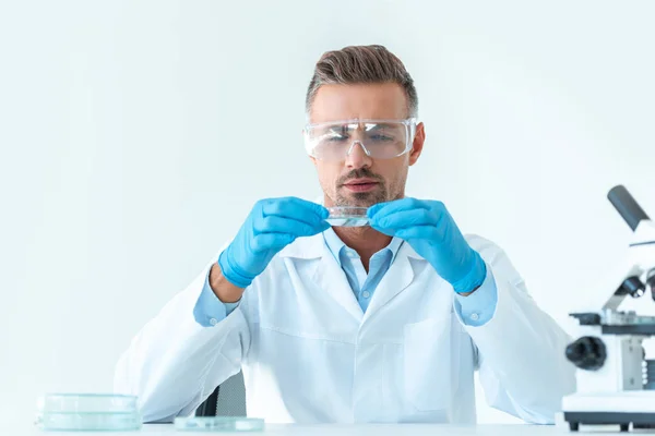 Gutaussehender Wissenschaftler in Schutzbrille betrachtet Reagenz während des Experiments isoliert auf weiß — Stockfoto