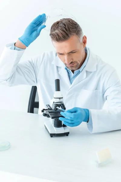 Schöner Wissenschaftler mit Schutzbrille und Blick auf Mikroskop isoliert auf weiß — Stockfoto